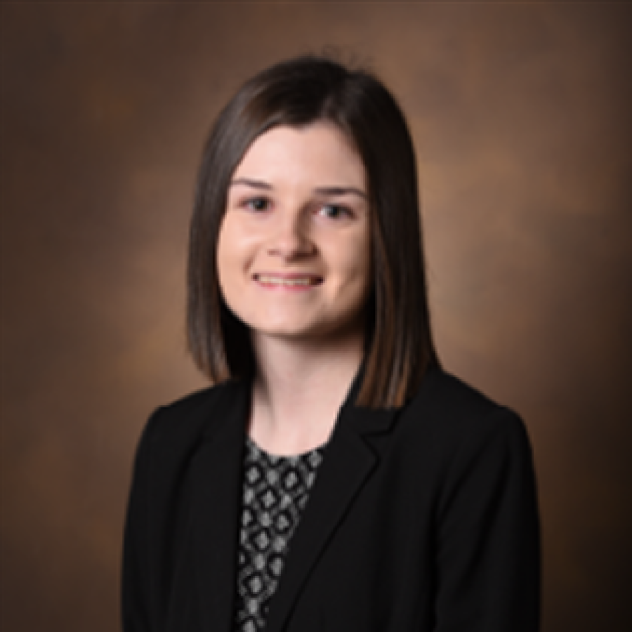 Headshot of white woman with straight shoulder-length brown hair, patterned shirt, and dark blazer