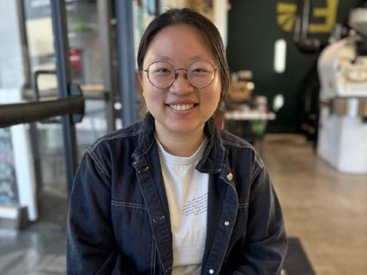 Asian woman in denim jacket seated at a cafe table. Photo by Lisa Levoir.