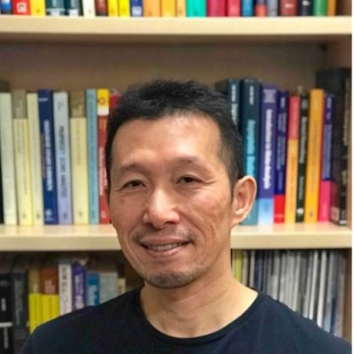 Headshot of Hajime Uno, PhD - Japanese American man standing in front of bookshelf
