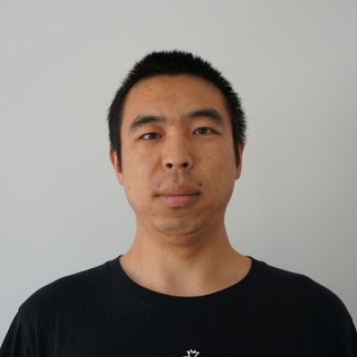 Headshot of Asian man with short black hair in black t-shirt against white background