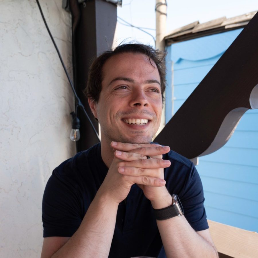 Man in navy blue t-shirt sitting in corner with chin on hands, grinning
