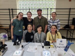 Ann Tate's lab group at MegaMicrobe 2019. Group smiling behind a white table with microscopes