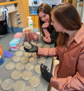 Woman holds petri dish for a female student to see