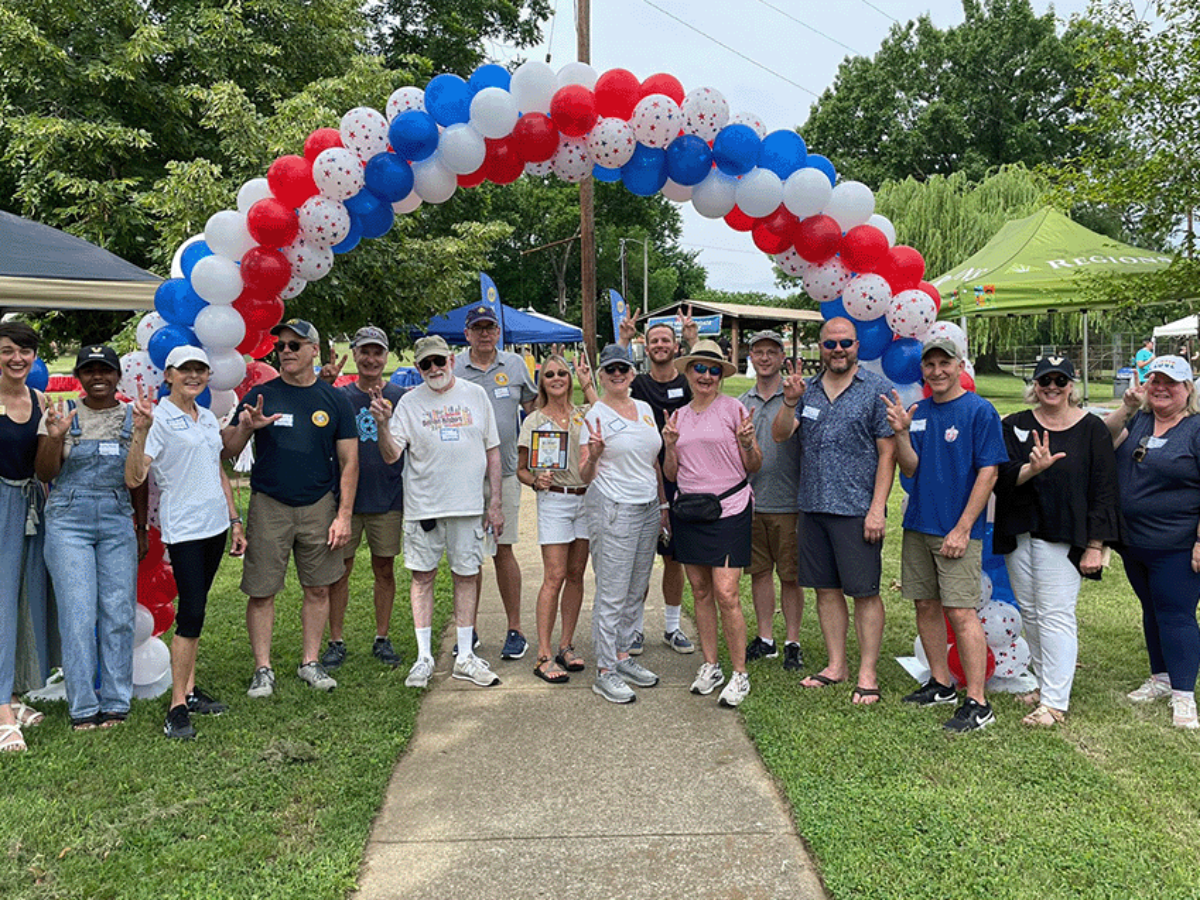 group photo of community members in a park under a patriotic balloon arch